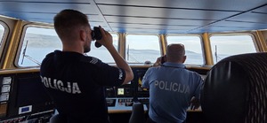 dwaj policjanci płyną łódką i patrzą przez lornetki