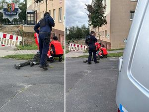 policjant pochylony nad ratownikami medycznymi udzielającymi pomocy mężczyźnie leżącemu na drodze