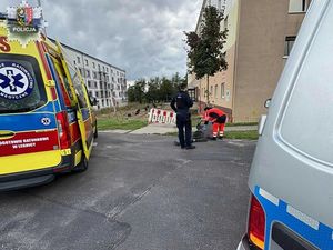 policjant pochylony nad ratownikami medycznymi udzielającymi pomocy mężczyźnie leżącemu na drodze obok karetka i radiowóz