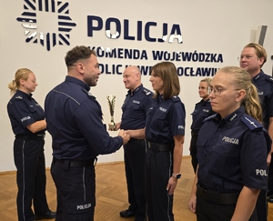 Zastępca Komendanta podaje rękę policjantce, w tle pozostali policjanci
