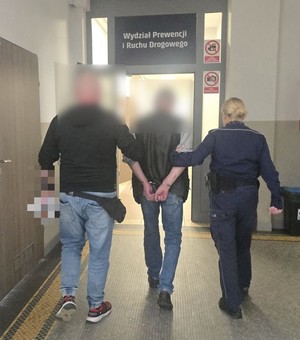 daj policjanci po cywilu prowadzą zatrzymanego skutego w kajdanki