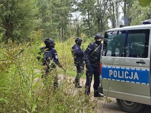 policjanci w pełnym umundurowaniu ćwiczebnym wsiadają do radiowozu stojącego w lesie
