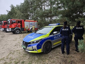 policjantki obok radiowozu dalej wozy strażackie i strażacy