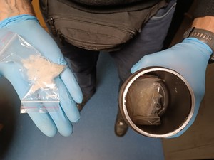 policjant trzyma w prawej ręce na której ma rękawiczkę woreczek z amfetaminą w lewej ręce trzyma pojemnik w którym się znajdował woreczek