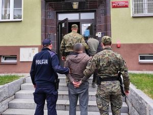 policjant i dwóch  funkcjonariuszy straży granicznej  prowadzą dwóch zatrzymanych do jednostki Straży Granicznej