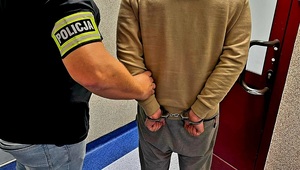 policjant prowadzi zatrzymanego skutego w kajdanki