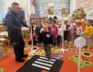Policjant pokazuje chłopcu ja sztucznych pasach jak bezpiecznie przechodzić przez pasy