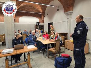 policjant przemawia do siedzących na sali seniorów