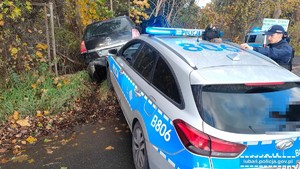 dwa radiowozy a przed nimi samochód po kolizji z drzewem