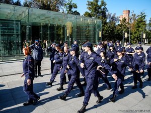 Na zdjęciu widocznie są młodzi ludzie w granatowych mundurach idący grupą na placu