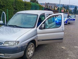 srebrny samochód osobowy z otwartymi drzwiami, za autem radiowóz