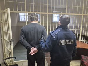 policjant prowadzi zatrzymanego za kraty