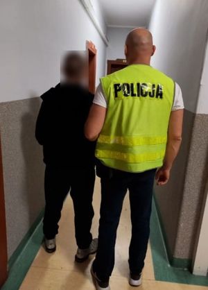 Policjant w cywilu z kamizelką odblaskową z napisem policja prowadzi zatrzymanego