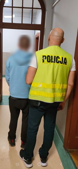 zatrzymanego w niebieskiej bluzie prowadzi policjant nieumundurowany w kamizelce odblaskowej