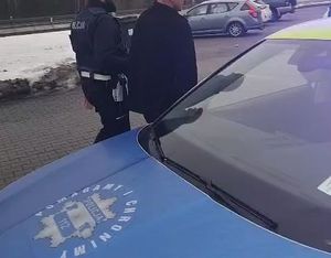 policjant prowadzi nietrzeźwego kierowcę do radiowozu