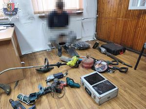 zatrzymany siedzący akuty w kajdanki na krześle przed nim rozłożone skradzione elektronarzędzia