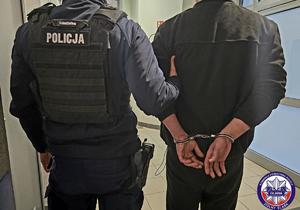 policjant prowadzi zatrzymanego skutego w kajdanki