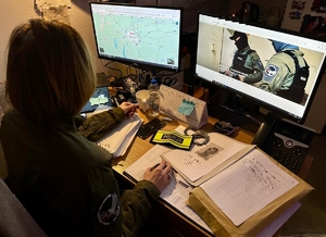 Policjantka Wydziału Poszukiwań i Identyfikacji Osób Komendy Wojewódzkiej Policji we Wrocławiu siedząca przy biurku przed dwoma monitorami