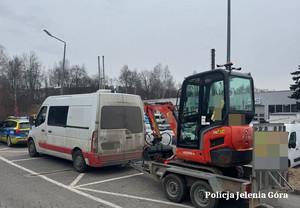radiowóz, a  za nim biały bus z przyczepką z koparką