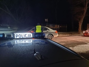 radiowóz i policjant zatrzymujący kierowcę samochodu osobowego