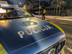 radiowóz, a za nim policjant kontrolujący ruch drogowy na ulicy
