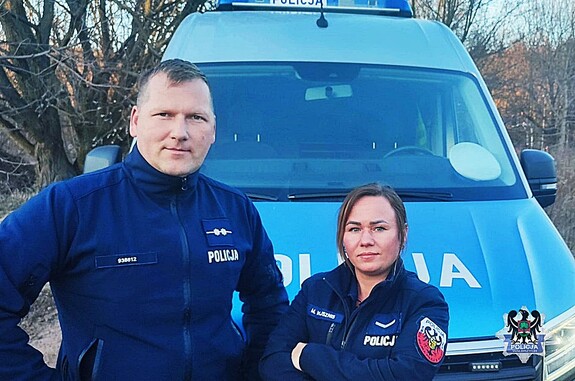 Policjanci w mundurach na tle radiowozu