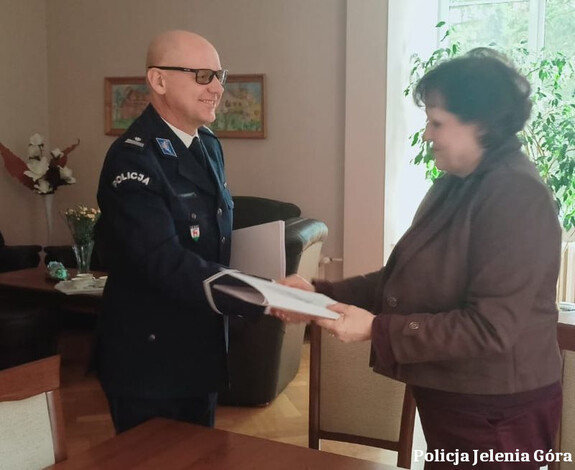 policjant podaje rękę i przekazuje dokument kobiecie