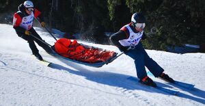 dwaj narciarze podczas konkurencji zwożą człowieka na noszach z góry