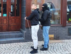 policjant z zatrzymanym skutym w kajdanki zespolone