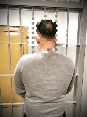 zatrzymany mężczyzna stojący tyłem do obiektywu, a przodem do krat