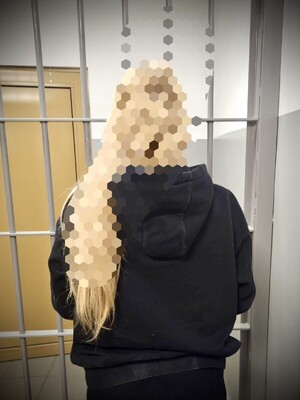 zatrzymana kobieta stojąca tyłem do obiektywu, a przodem do krat