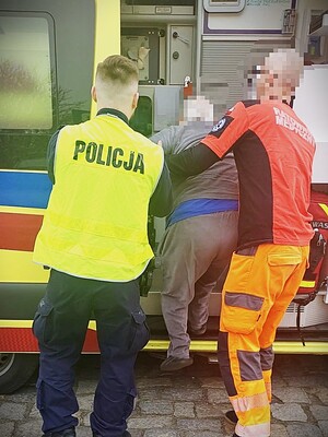 policjant i medyk pomagają starszemu mężczyźnie wsiadać do karetki