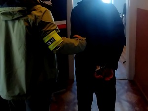 policjant prowadzi osobę zatrzymaną skutego w kajdanki