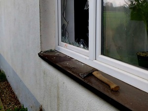 wybita szyba w oknie oraz widoczna siekiera na parapecie