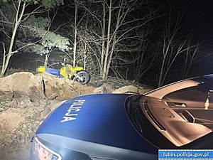 Na pierwszym planie radiowóz, a w tle leżący na poboczu drogi leśnej motocykl