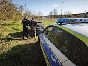 radiowóz a za nim policjanci z zatrzymanym