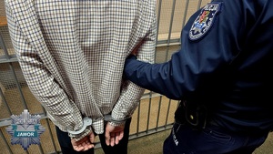 policjant prowadzi zatrzymanego skutego w kajdanki