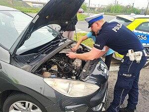 Policjant z kierującą przy pojeździe z otwartą maską