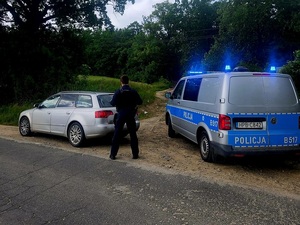 policjant stojący pomiędzy samochodem osobowym a radiowozem stojącymi na poboczu
