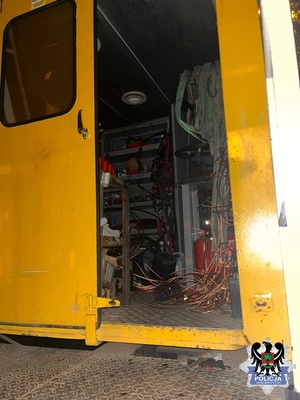 Wnętrze drezyny kolejowej. Widać uchylone drzwi koloru żółtego, na podłodze znajdują się elektronarzędzia i miedziane przewody.