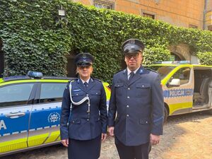 Umundurowani policjanci stoją przed radiowozem służbowym.