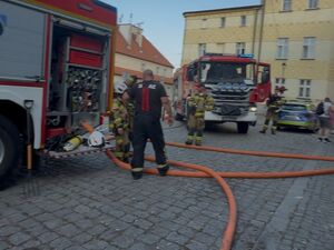 Strażacy rozwijają węże z wozu bojowego zaparkowanego na osiedlu.