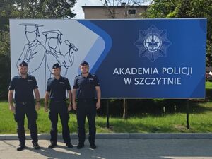Trzech umundurowanych policjantów stoi na tle dużego baneru z napisem Akademia Policyjna.