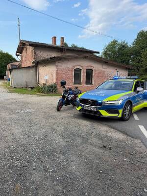 Radiowóz policyjny i motocykl. Oba pojazdy są zaparkowane w pobliżu domu przy jezdni.