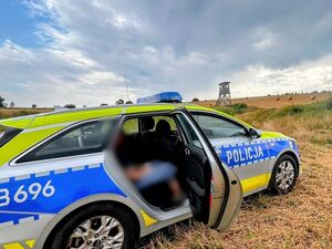 Policyjny radiowóz zaparkowany jest w polu, w oddali widać ambonę myśliwską.