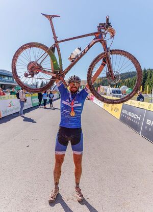 kolarz po wyścigu trzymający rower w górze w geście zwycięstwa
