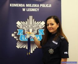 Na zdjęciu policjantka pozuje ze zdobytymi medalami na tle baneru Komendy Miejskiej Policji w Legnicy