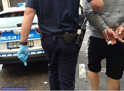Policjant prowadzi zatrzymanego mężczyznę w kajdankach