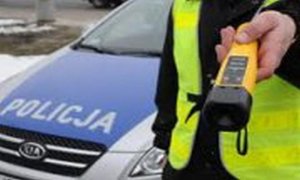Policjant przy radiowozie trzyma w rękach alkomat