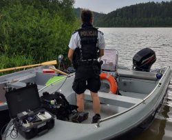 Policjant z Komisariatu Wodnego stojący na łodzi policyjnej przycumowanej do brzegu akwenu wodnego przed rozpoczęciem patrolu